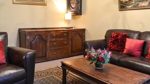 A living room with a dark leather sofa, a wooden cabinet, and a coffee table with a floral arrangement. - 4 bedroom accommodation in Easingwold, near York (Easingwold, near York)