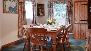 A dining room with a wooden table set for six, surrounded by chairs. There is a bookshelf to the left and a wooden cabinet to the right. - 4 bedroom accommodation in Easingwold, near York (Easingwold, near York)