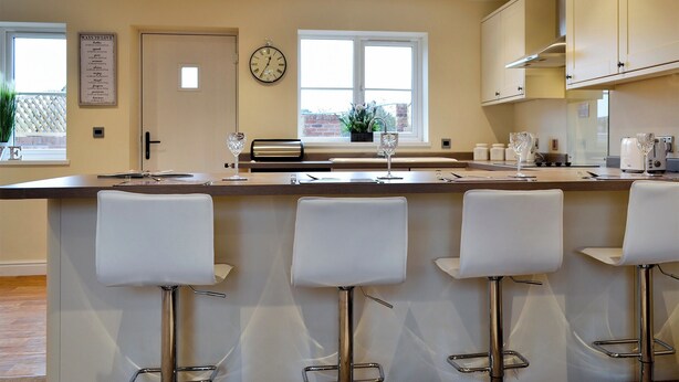 Une cuisine moderne avec un coin bar, des tabourets de bar blancs, une horloge et une fenêtre donnant sur un beau paysage.