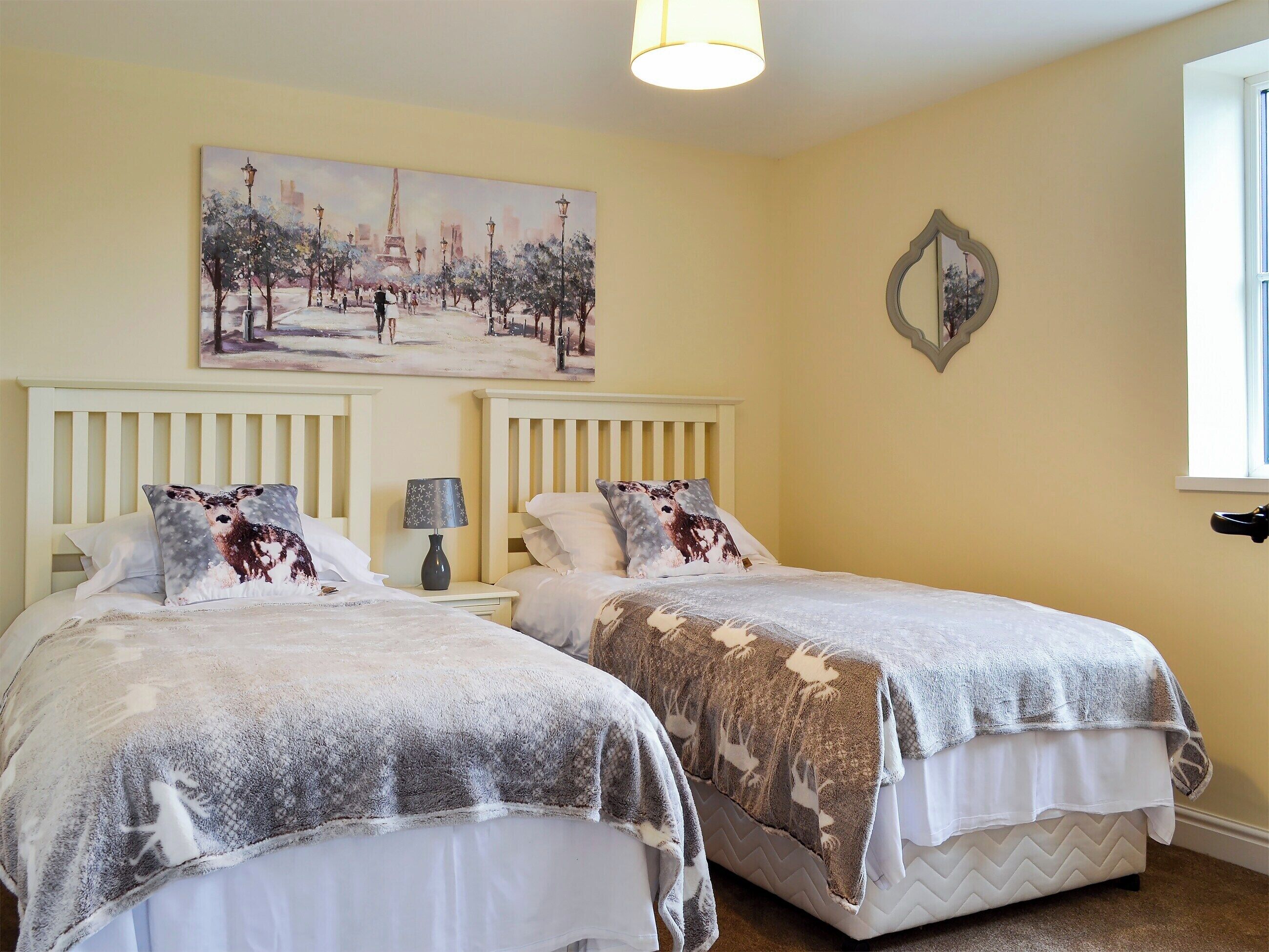 A bedroom with two beds, a painting of a park scene, a lamp, and a decorative mirror.