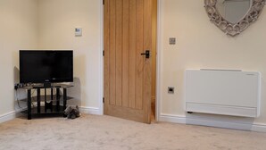 Une pièce avec une porte en bois, un téléviseur posé sur un meuble, un radiateur et un miroir décoratif en forme de cœur accroché au mur.
