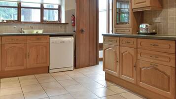 A kitchen with wooden cabinets, a dishwasher, a window with curtains, and a tiled floor.