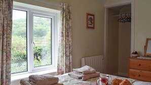 A bedroom with a bed, a radiator, a window with curtains, a bedside table with a bowl of fruit and a cup, and a wooden dresser. - 3 bedroom accommodation in Grosmont, near Whitby (Grosmont, near Whitby)