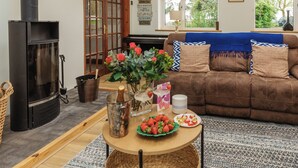 A cozy living room with a fireplace, a sofa, a coffee table with strawberries, and a view of the outdoors.
