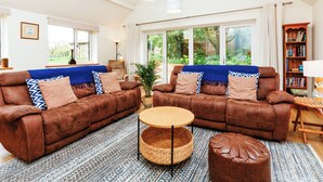 A spacious living room with two brown leather sofas, a round coffee table, and a large window offering a view of greenery.