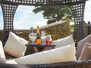 Eine Sitzgruppe aus Rattan im Freien mit einer Steinsandsteinmauer im Hintergrund, einer Champagnerflasche und Erdbeeren auf einem kleinen Tisch.