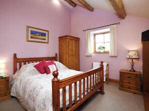A bedroom with a wooden bed, a wardrobe, a window with curtains, a bedside lamp, and a framed picture on the wall.