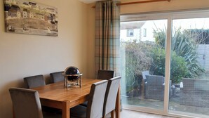 Un coin repas avec une table en bois et six chaises, un globe terrestre en guise de décoration centrale et une grande fenêtre donnant sur un jardin et des maisons.