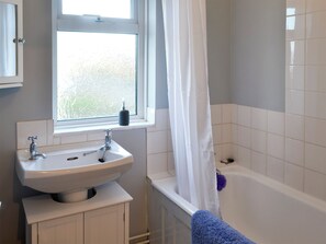 Une salle de bain avec un lavabo blanc, une fenêtre à verre dépoli, une baignoire et une serviette bleue.