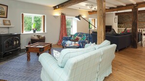 A cozy living room with a fireplace, a sofa, a patterned rug, and a window with curtains. - 5 bedroom accommodation in Llansilin, near Oswestry (Llansilin, near Oswestry)