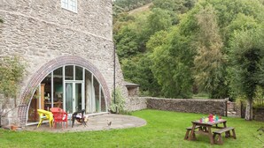 A stone building with a curved glass door, a patio with chairs, and a picnic table. - 5 bedroom accommodation in Llansilin, near Oswestry (Llansilin, near Oswestry)