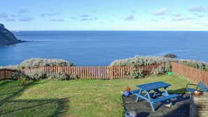A patio with a view of the ocean, a wooden fence, and a blue picnic table. - 3 bedroom accommodation in Gardenstown, near Macduff (Gardenstown, near Macduff)