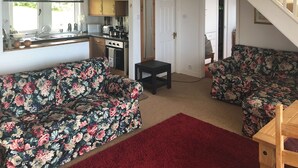 A compact living space with a kitchenette, two floral-patterned sofas, a red rug, and a staircase. - 3 bedroom accommodation in Gardenstown, near Macduff (Gardenstown, near Macduff)