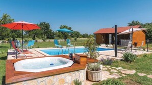 Une piscine avec des chaises longues et des parasols, un jacuzzi et un chalet en bois.