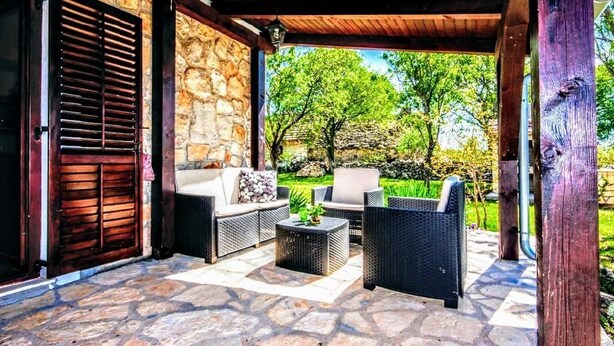 Un espace extérieur aménagé en terrasse, avec des meubles en osier, un mur en pierre et une vue sur la verdure.