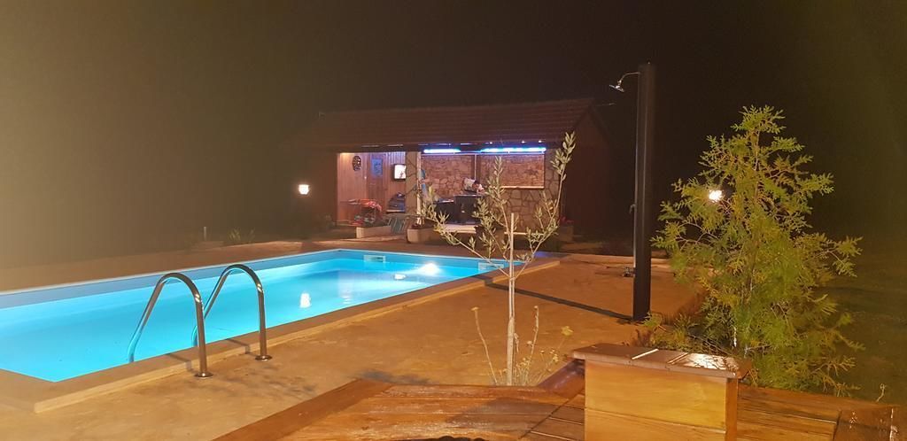 Una piscina nocturna con zona de patio y un edificio al fondo.