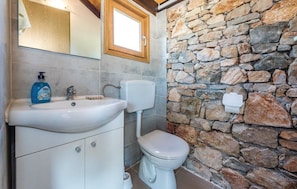 A bathroom with a stone wall, a sink, a toilet, and a mirror.