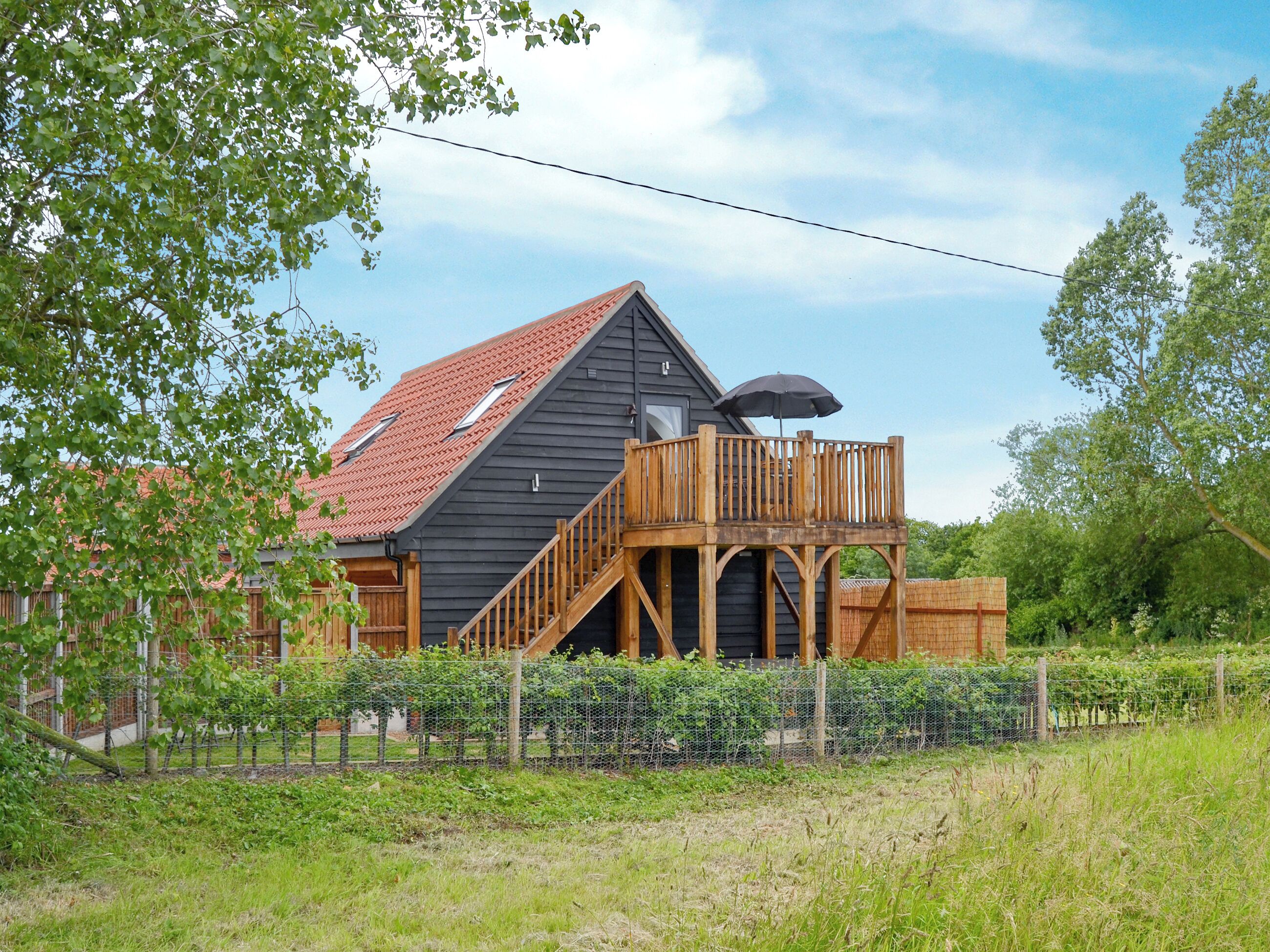 A house with a wooden deck, a red roof, and a fenced garden area.