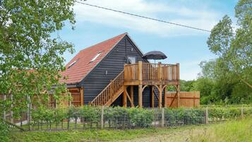 A house with a wooden deck, a red roof, and a fenced garden area.