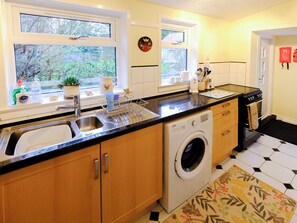 A compact kitchen with a washing machine, a sink, and a window with a view of greenery. - 2 bedroom accommodation in Balintore, near Tain (Balintore, near Tain)