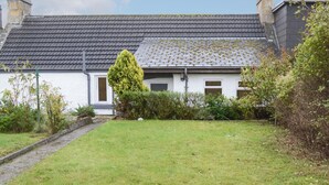 Une maison avec un toit en tuiles, une porte d’entrée et un petit jardin devant, avec un chemin menant à la porte.