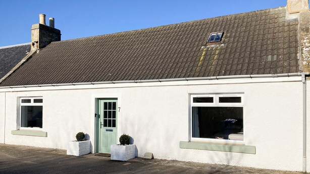 Un bâtiment blanc avec une porte verte, deux fenêtres et une petite lucarne.
