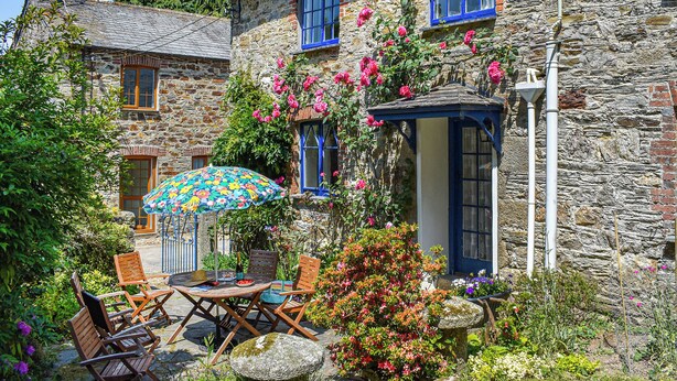 Ein Haus aus Stein mit Gartenpatiо, einer blauen Tür und einem Blumenkasten.