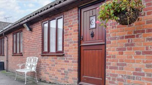 A brick building with a wooden door, windows, and a bench outside. - Stable Cottage 1 - UKC3741 (Foxley, near Fakenham)