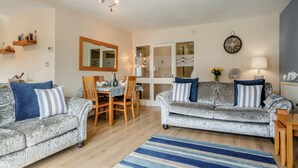 A living room with two grey sofas, a dining table with chairs, a blue striped rug, and a chandelier. - 2 bedroom accommodation in Beadnell, near Seahouses (Beadnell, near Seahouses)