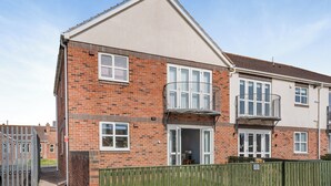 A two-story residential building with a brick facade, white-framed windows, and a green fence. - 2 bedroom accommodation in Beadnell, near Seahouses (Beadnell, near Seahouses)