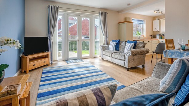 A spacious living room with a large TV, a sofa, a dining table, and a kitchen area visible through an open door. - 2 bedroom accommodation in Beadnell, near Seahouses (Beadnell, near Seahouses)
