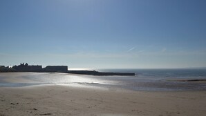 A beach with a clear sky, calm sea, and a distant shoreline with buildings. - 2 bedroom accommodation in Beadnell, near Seahouses (Beadnell, near Seahouses)