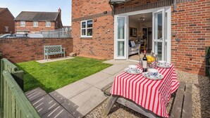 A patio with a table set for tea, a brick house, and a lawn. - 2 bedroom accommodation in Beadnell, near Seahouses (Beadnell, near Seahouses)