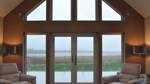 A spacious room with a high ceiling, large windows, and two leather chairs. - 2 bedroom accommodation in Clachan Sands, Isle of North Uist (Clachan Sands, Isle of North Uist)