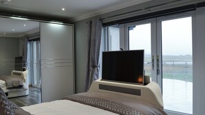 A modern hotel room with a large bed, a flat-screen TV, a balcony with a view, and a large mirror. - 2 bedroom accommodation in Clachan Sands, Isle of North Uist (Clachan Sands, Isle of North Uist)