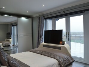 Quarto de hotel moderno com uma cama grande, televisão de tela plana, varanda com vista e um espelho grande.