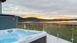 A hot tub on a balcony with a view of a sunset over a lake and hills. - 2 bedroom accommodation in Clachan Sands, Isle of North Uist (Clachan Sands, Isle of North Uist)