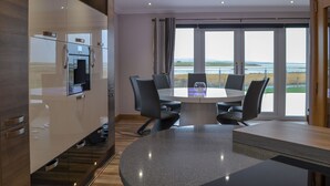 A modern kitchen with built-in appliances, a dining area with a table and chairs, and a large window offering a view of the sea. - 2 bedroom accommodation in Clachan Sands, Isle of North Uist (Clachan Sands, Isle of North Uist)
