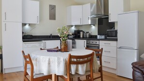 Une cuisine compacte avec des meubles blancs, un îlot central doté de chaises, une horloge au mur et des appareils électroménagers modernes.