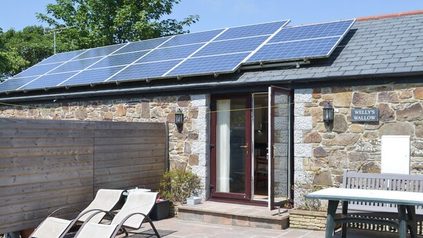 Un bâtiment doté d’une façade en pierre, d’une clôture en bois et d’une installation de panneaux solaires sur le toit.
