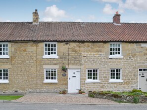 Un bâtiment en pierre avec un toit recouvert de tuiles, de nombreuses fenêtres et une porte.