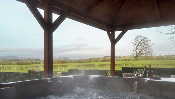 Een jacuzzi-gedeelte met uitzicht op een groen landschap, stenen muren en een houten pergola.