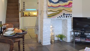 A living room with a staircase, a dining area with a table set for two, a flat-screen TV, and a bookshelf. - 2 bedroom accommodation in Brixham (Brixham)