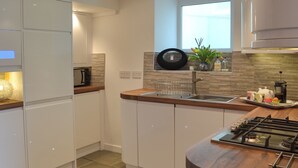 A modern kitchen with white cabinets, a wooden countertop, a gas stove, a sink, and a window above the sink. - 2 bedroom accommodation in Brixham (Brixham)