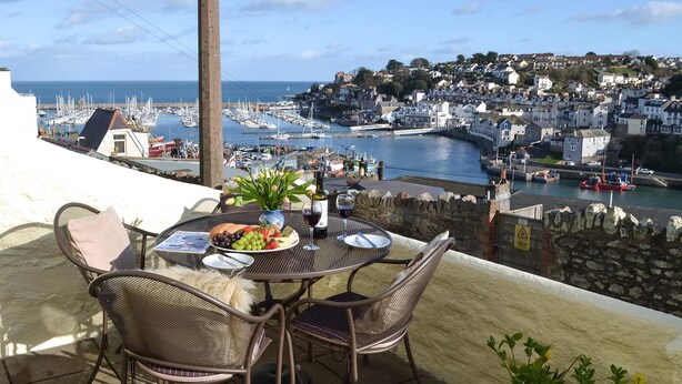 An outdoor dining area with a table set for two, overlooking a marina and a coastal town. - 2 bedroom accommodation in Brixham (Brixham)