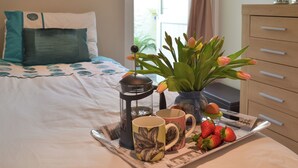A neatly made bed with a blue and white patterned bedspread, a bedside table with a teapot, two mugs, a tray with strawberries, and a vase with tulips. - 2 bedroom accommodation in Brixham (Brixham)