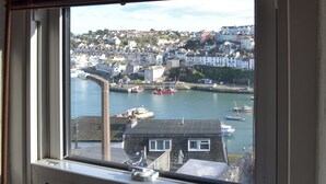 A coastal town view from a window, including a harbor with boats, a prominent chimney, and residential buildings. - 2 bedroom accommodation in Brixham (Brixham)