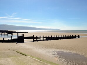 A beach with a wooden fence, a pier, and a distant mountain.