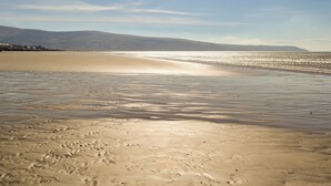 Una playa con huellas, cielo despejado y montañas a lo lejos.