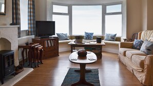 Una sala de estar con chimenea, televisor, sofá y vistas amplias a través de grandes ventanales.